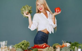 Cheerful woman in white shirt holding lettuce and pepper, celebrating fresh vegetables.